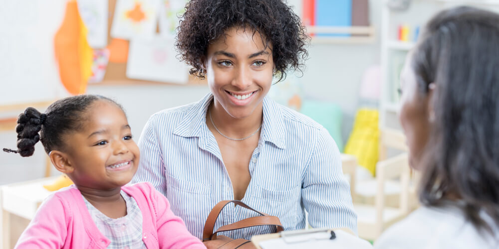 A teacher hosts a parent teacher conference with a smiling mom and her child