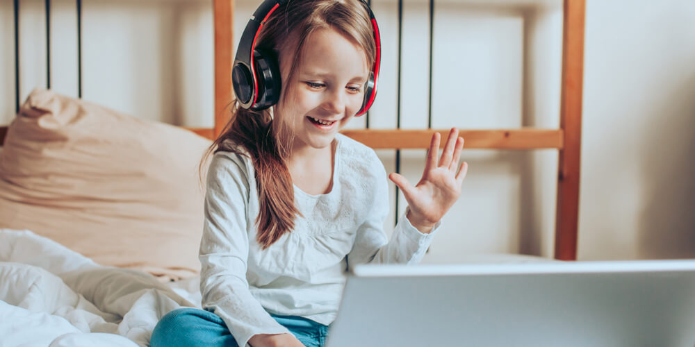 An elementary school student smiles and waves while attending a virtual class on her laptop
