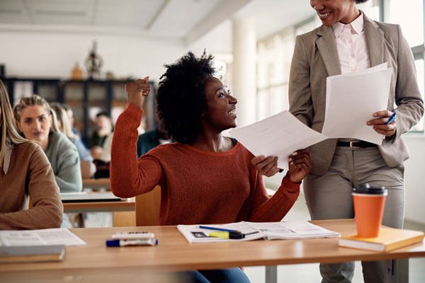 Teacher passing out graded papers and female high school student celebrating her score