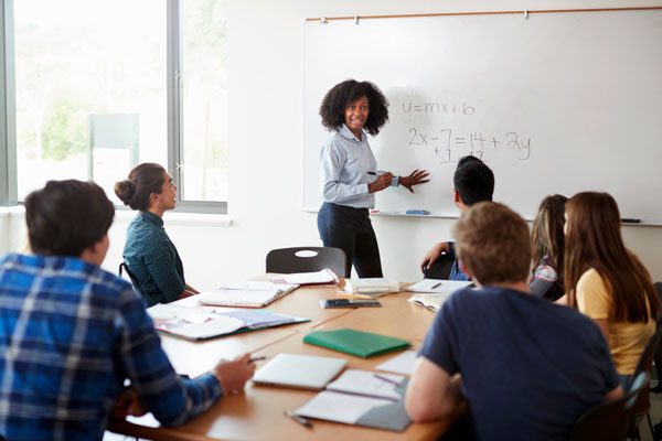 Female high school teacher at whiteboard teaching math class