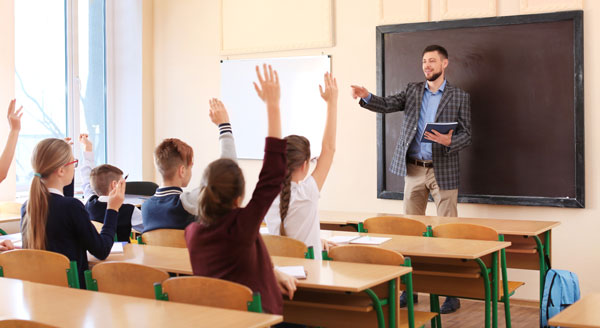 Students raising their hand while their teacher is at the chalk board