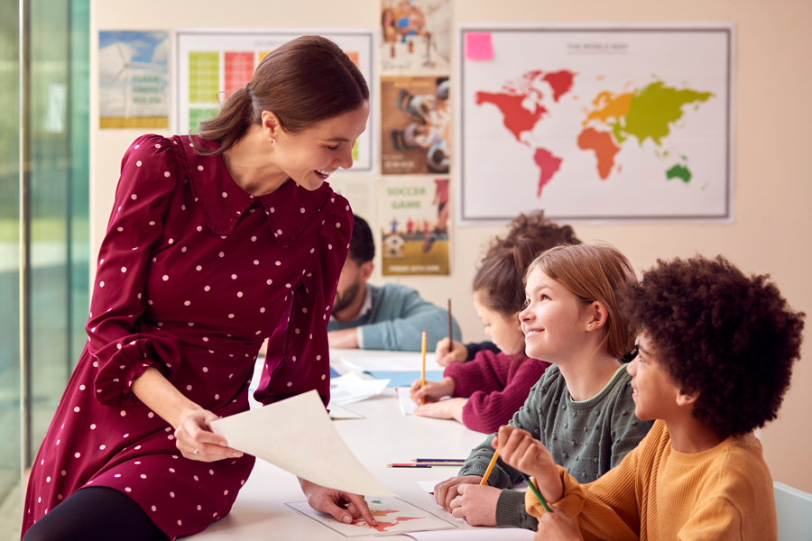 Smiling female elementary school teacher working at with students at their desk in the classroom