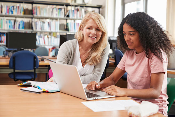 An educator working with a student on a laptop in the library